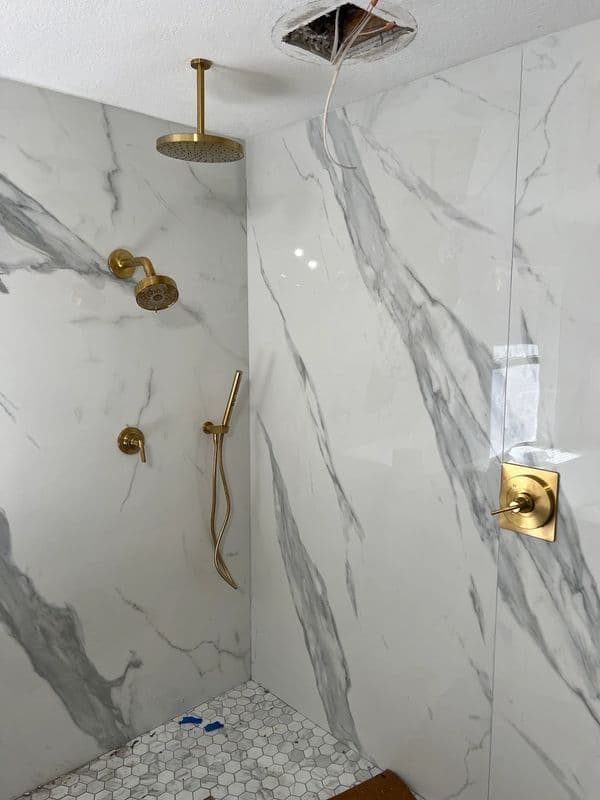Modern bathroom shower with gold fixtures and marble walls, featuring a ceiling repair.