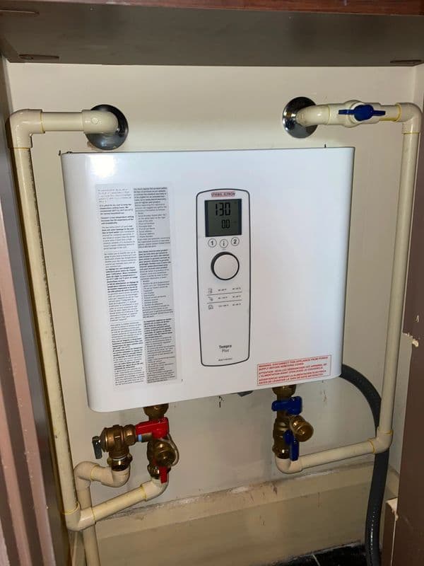 Tankless water heater installation with digital control panel and plumbing connections.