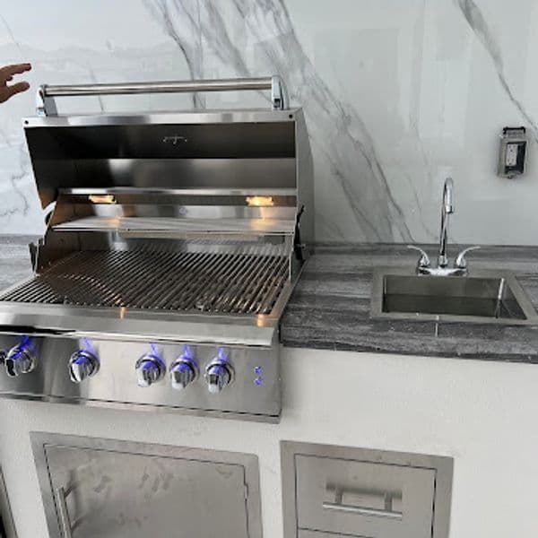 Stainless steel outdoor grill with open lid and modern countertop sink. Ideal for barbecuing.