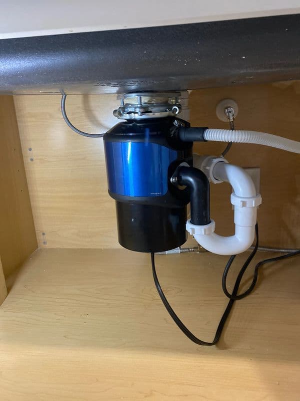 Under-sink garbage disposal unit with black and blue design, installed with white plumbing.
