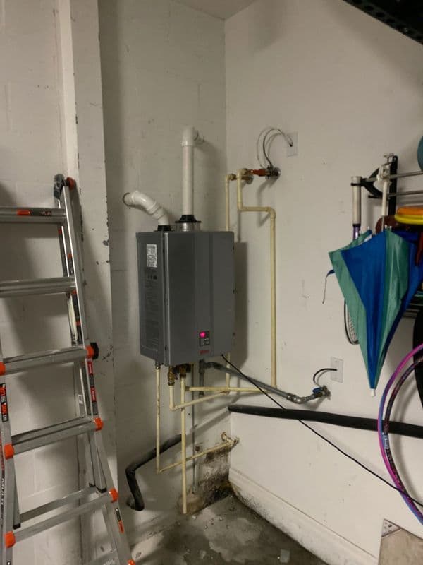 Tankless water heater installation in a garage with ladder and tools nearby.