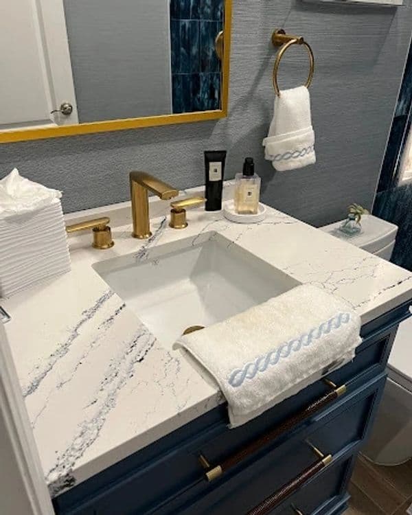 Modern bathroom vanity with white marble countertop, gold fixtures, and blue accents.