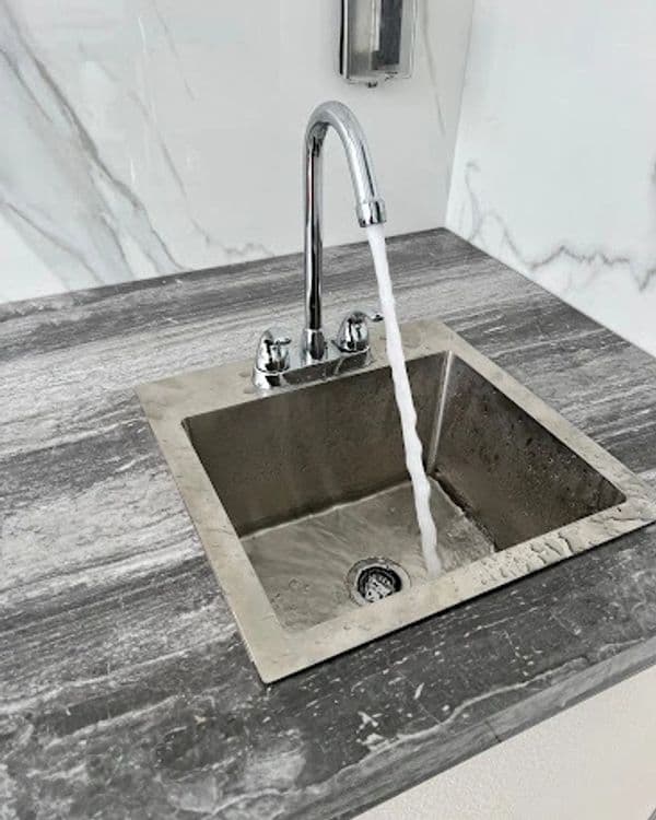 Modern stainless steel sink with running water on a marble countertop.