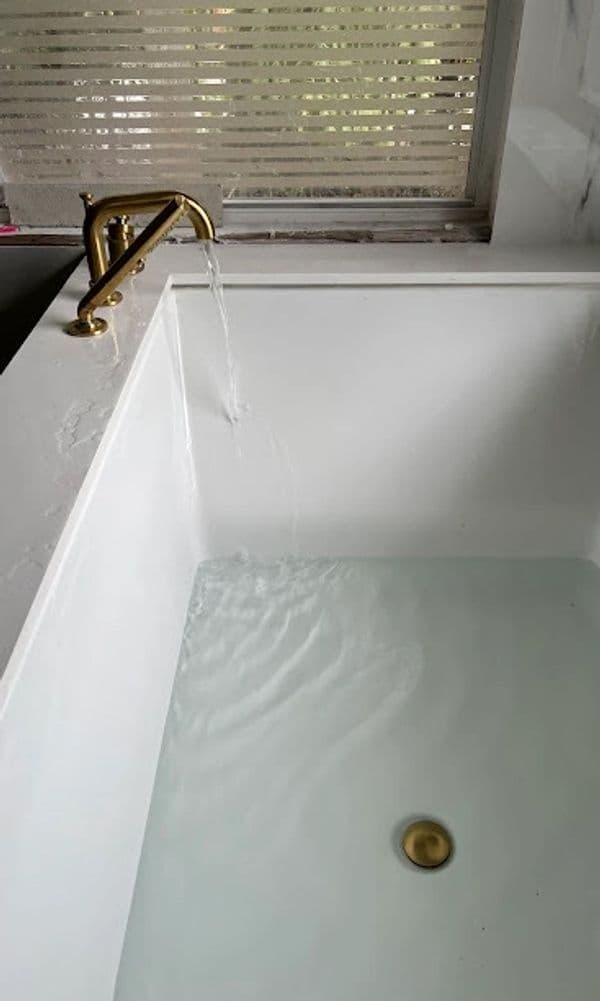 Luxury bathtub filling with water, featuring a gold faucet and serene atmosphere.