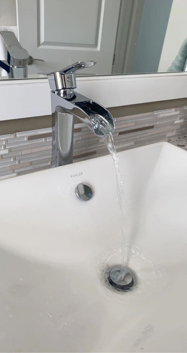 Modern bathroom sink with Kohler faucet flowing water into a white basin.