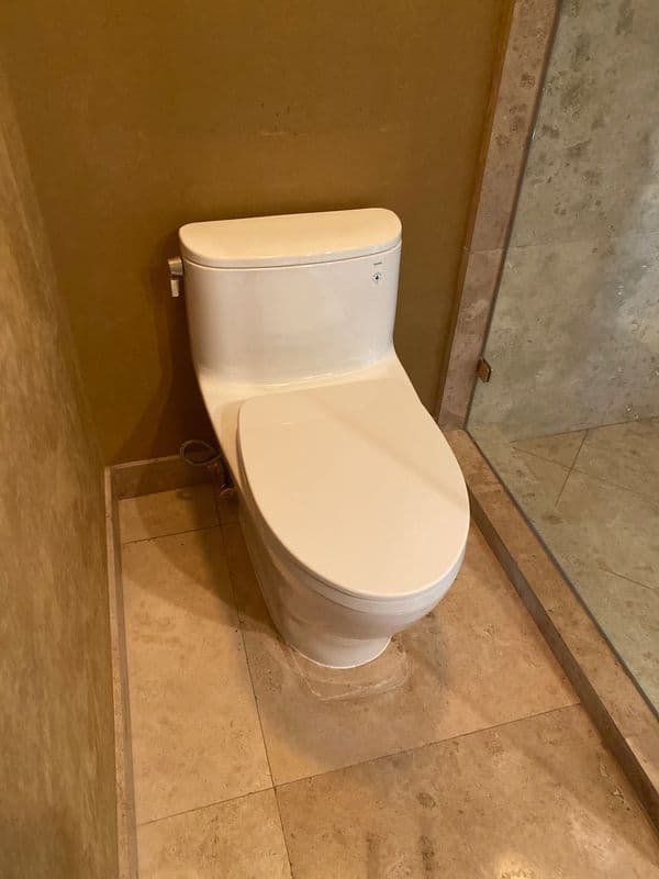 Modern toilet in a minimalist bathroom with stone tile flooring and a glass shower enclosure.