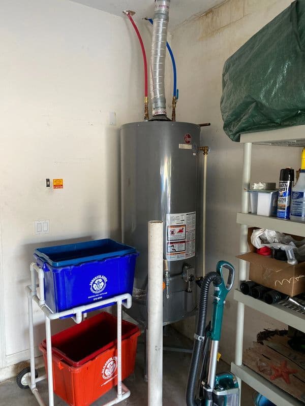 Water heater in garage with recycling bins and cleaning supplies nearby.