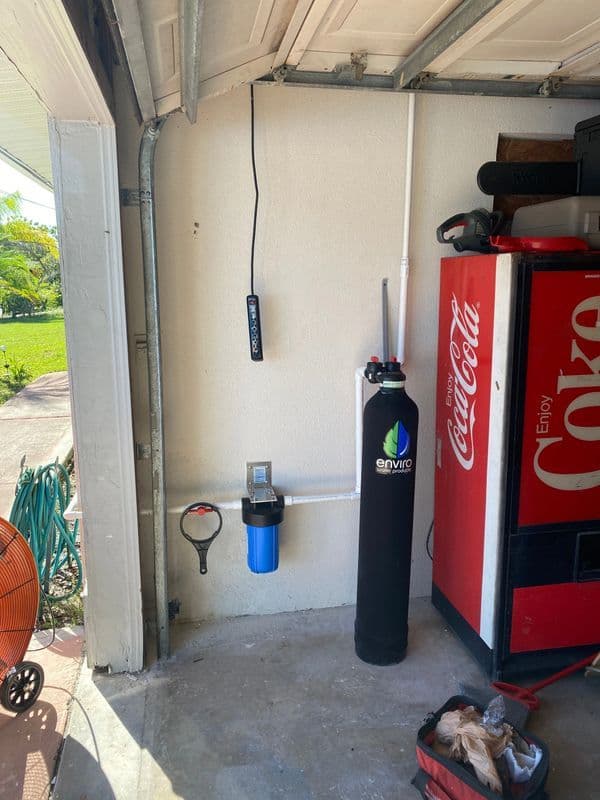 Water filtration system installation in a garage with a Coca-Cola vending machine nearby.