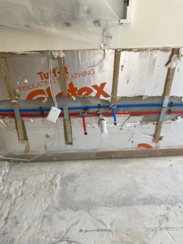 Exposed plumbing installation with red and blue pipes on insulated wall in a renovation setting.