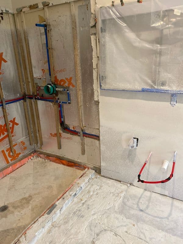 Bathroom renovation in progress with wall plumbing, insulation, and concrete flooring visible.