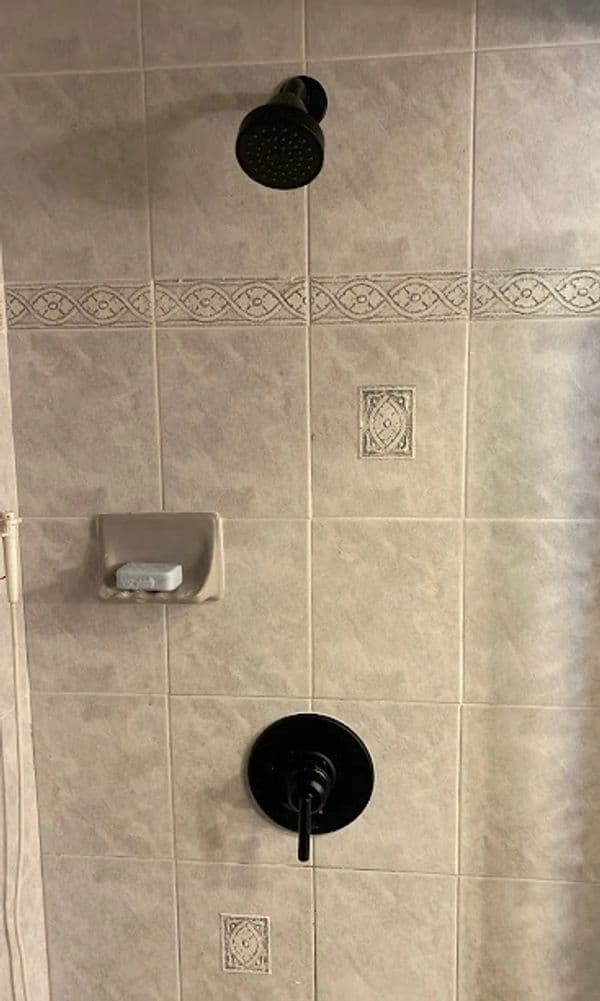 Modern shower with black faucet and overhead showerhead, set against decorative tile wall.