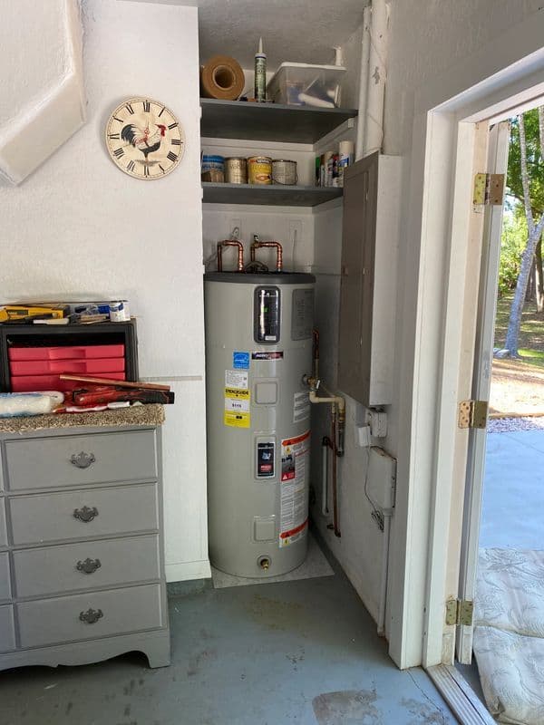 Water heater in garage with storage shelves and tools, featuring a clock on the wall.