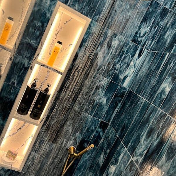 Elegant bathroom shower niche with blue marble tiles and stylish shampoo and conditioner bottles.