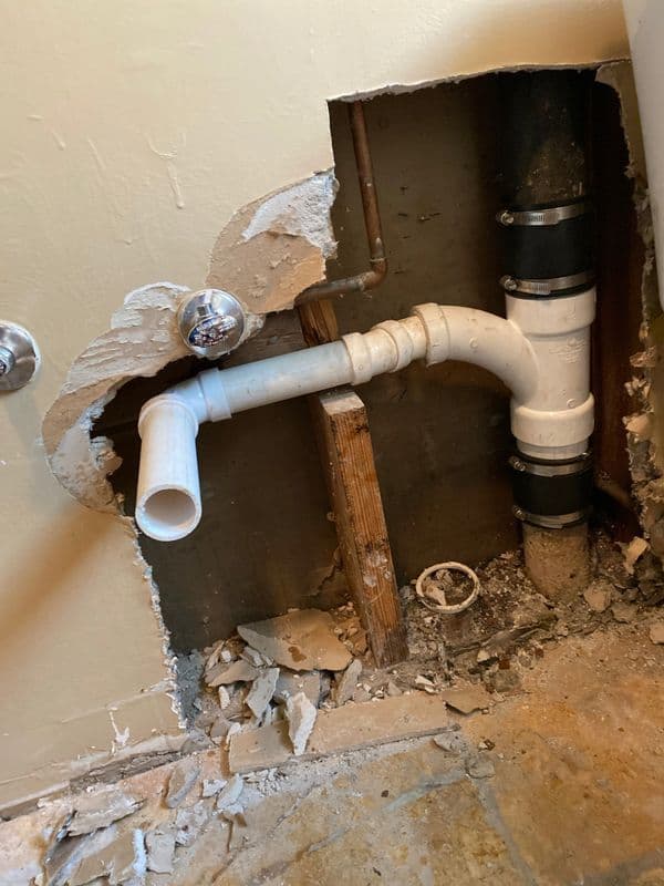 Exposed plumbing with damaged wall and PVC pipe connection in a bathroom renovation.