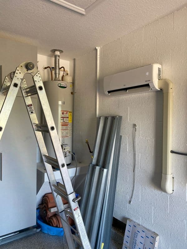 Ladder beside water heater and air conditioning unit in garage setting.