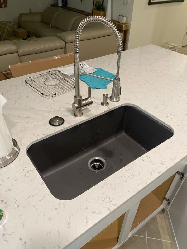 Modern kitchen sink with a sleek faucet on a white countertop, featuring a dark basin.