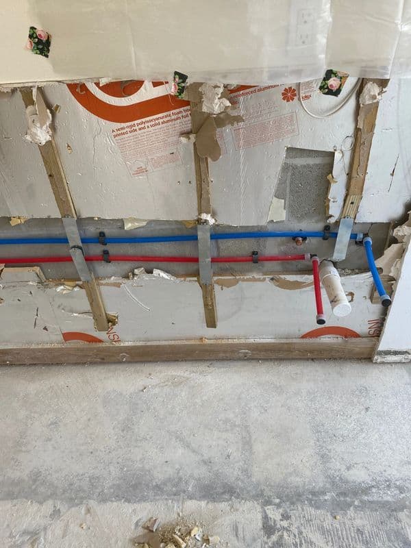 Exposed wall with plumbing pipes in red and blue, showing renovation progress.
