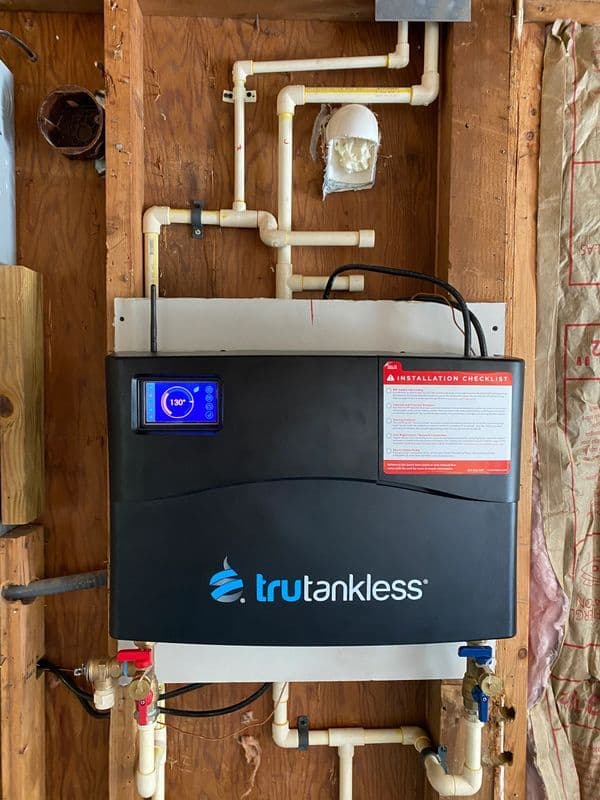 Trutankless electric water heater mounted on wall with installation checklist visible.