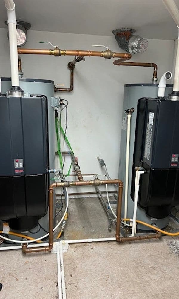 Two black water heaters connected by copper pipes in a utility room.