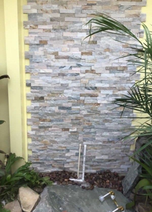 Textured stone wall with greenery and water features in a serene outdoor setting.