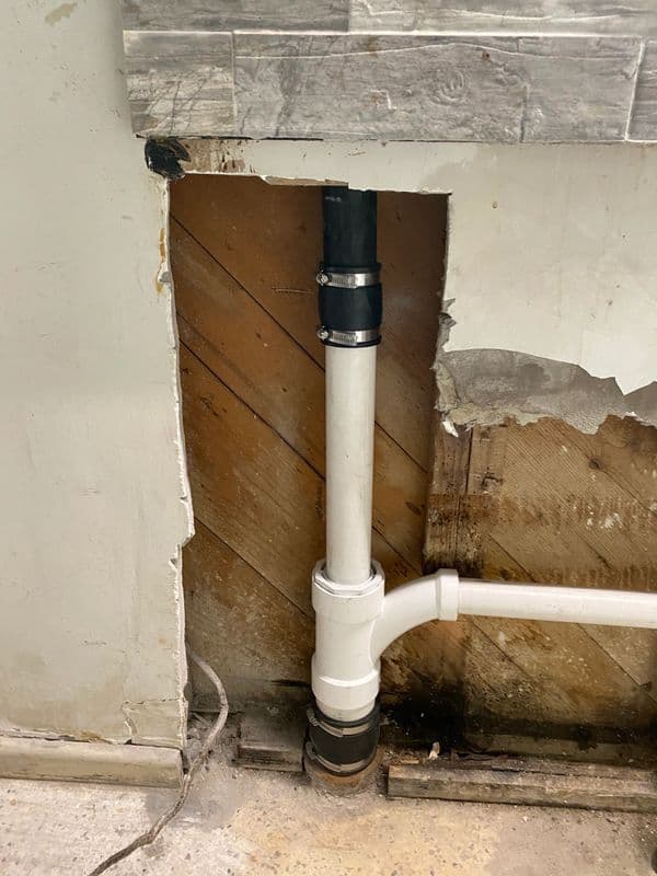 Damaged wall exposing plumbing pipes and water damage in a home renovation setting.