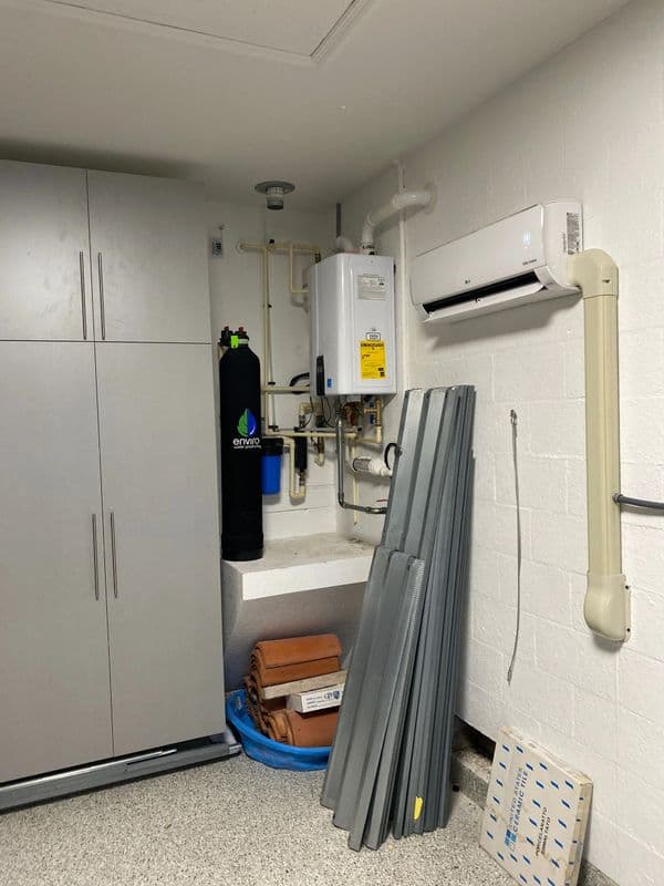 Water heater and air conditioning unit in a garage with storage cabinets and stacked panels.