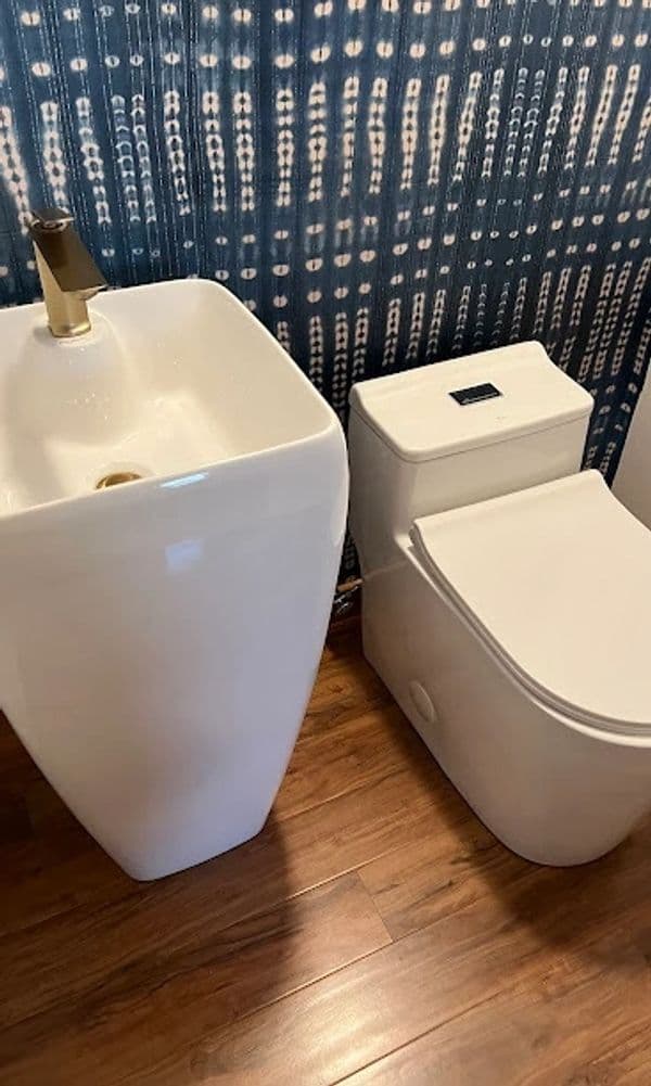 Modern bathroom setting featuring a sleek white sink and toilet against a blue patterned wall.