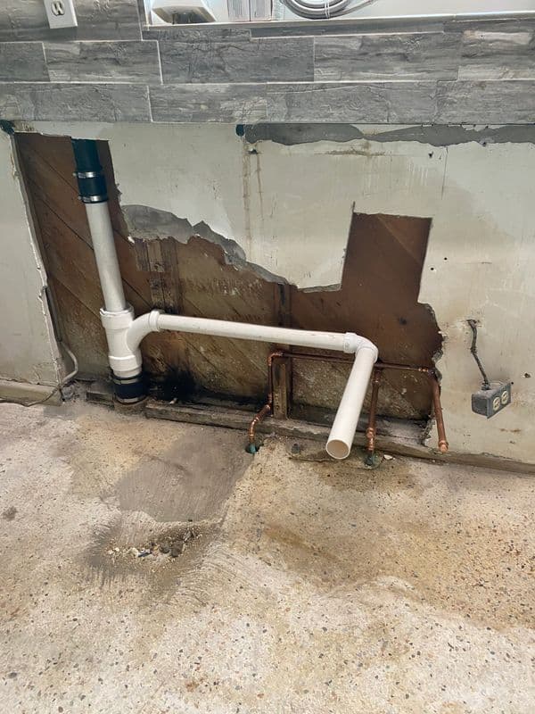 Damaged wall with exposed plumbing and pipes in a kitchen renovation site.