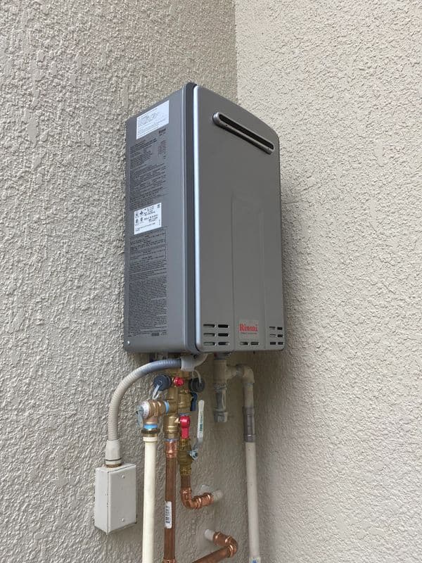 Tankless water heater mounted on a wall with plumbing connections visible.