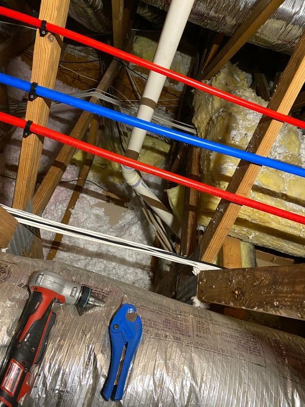 View of attic plumbing with pipes, insulation, and tools on beams.