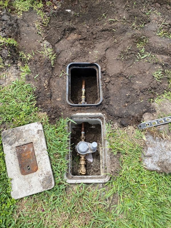 Water meter installation site with exposed valves in a grassy yard.
