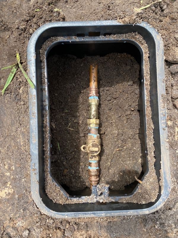 Valve box with a copper water valve and dirt, showing underground plumbing setup.