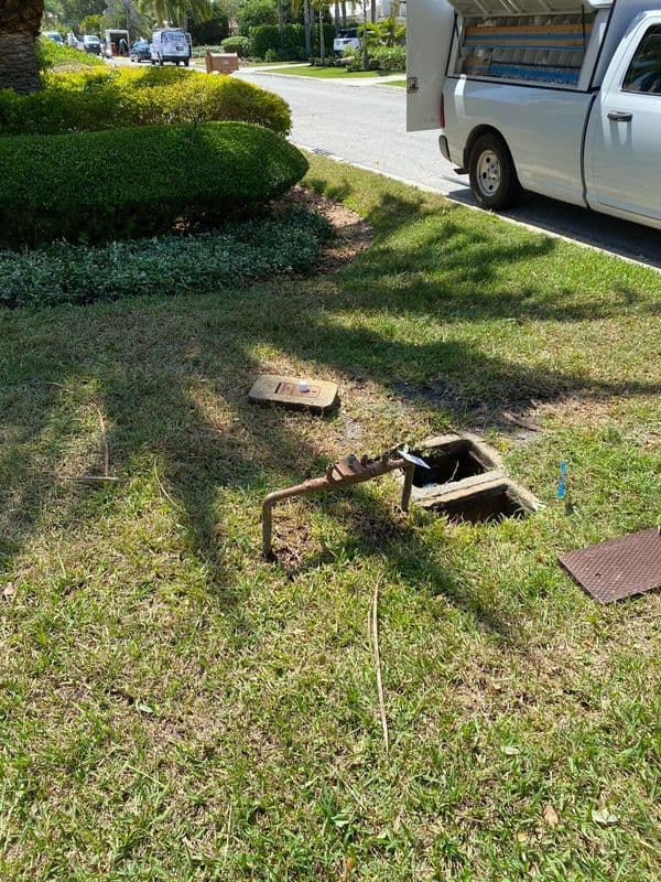 Sod and water meter in grassy area beside a parked white utility truck.