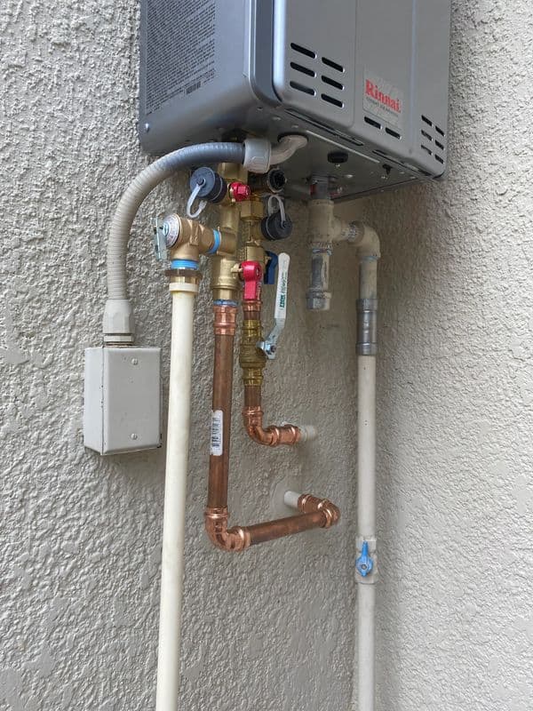 Rinnai tankless water heater with copper and PVC plumbing connections on exterior wall.