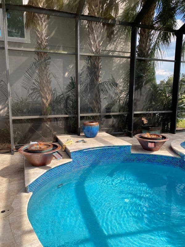 Stylish pool area with fire bowls, palm trees, and serene blue water, perfect for relaxation.