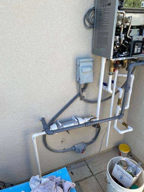 Water heater installation with pipes, valves, and electrical box mounted on a wall.