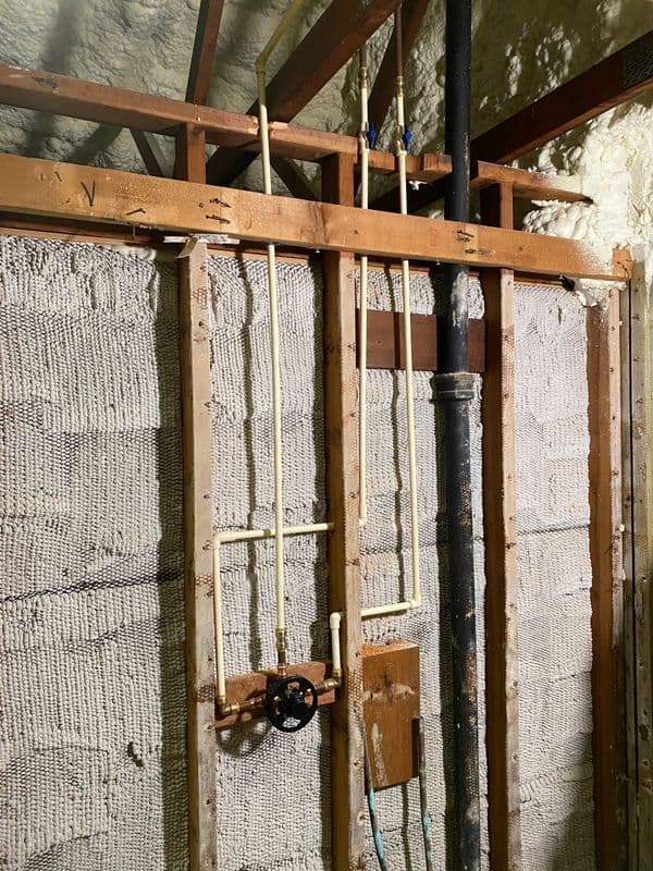 Exposed plumbing and piping in a partially constructed bathroom wall.