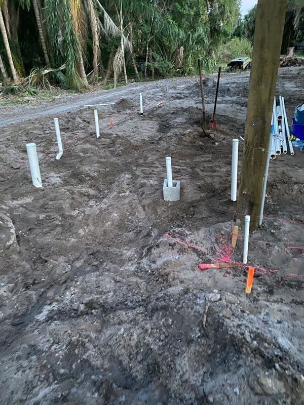 PVC pipes installed in muddy ground, surrounded by tools and vegetation. Construction site preparation.