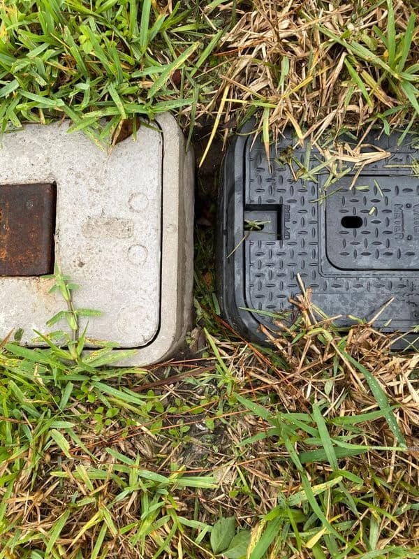 Adjacent utility access covers in grassy terrain, highlighting contrasting materials and textures.