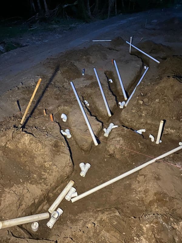 Excavated trench with white PVC pipes and fittings for plumbing installation at night.