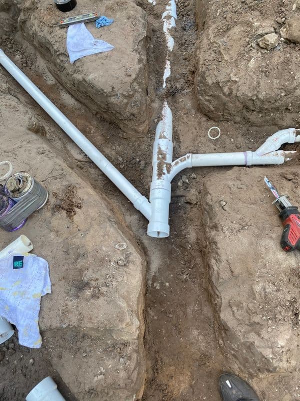 PVC piping installation in a trench with tools and materials visible.