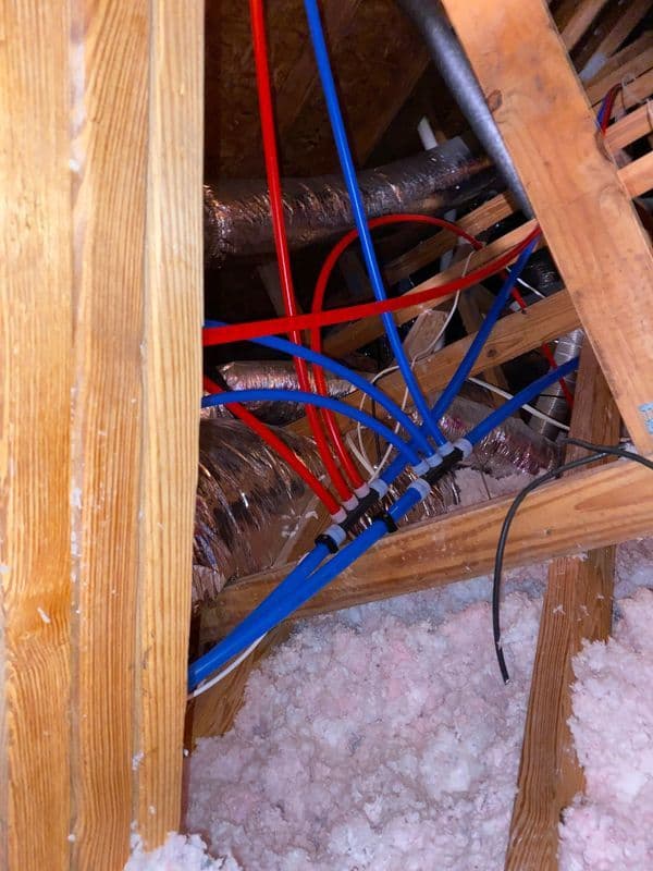 Colorful plumbing and wiring visible in an attic with insulation material below.