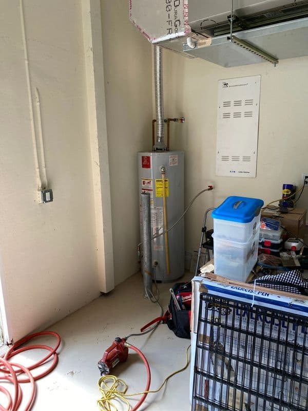Water heater installation in a utility room with tools and storage boxes.