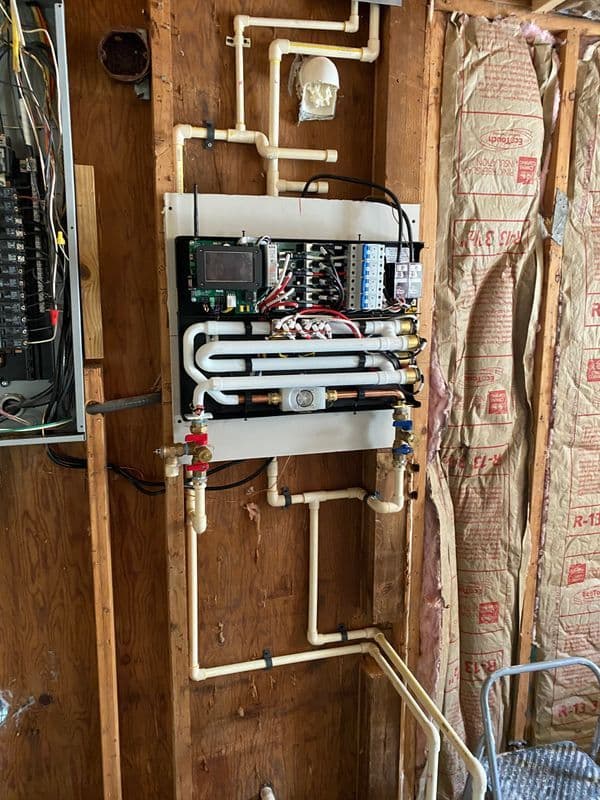 Plumbing control panel with piping and electrical connections in a construction setting.