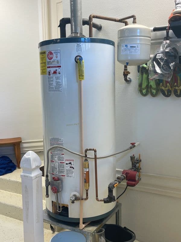 Water heater with pipes and valves, located in a utility area, surrounded by tools.