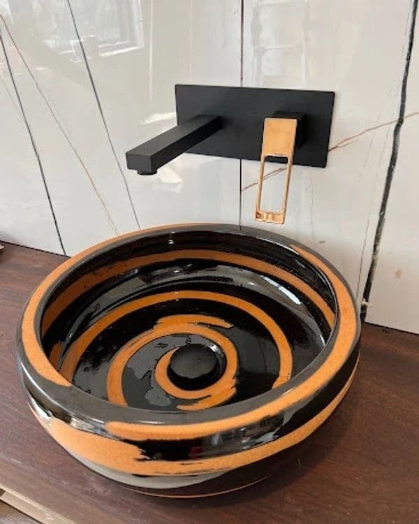 Modern black and orange spiral design sink with sleek black faucet against white tiled wall.