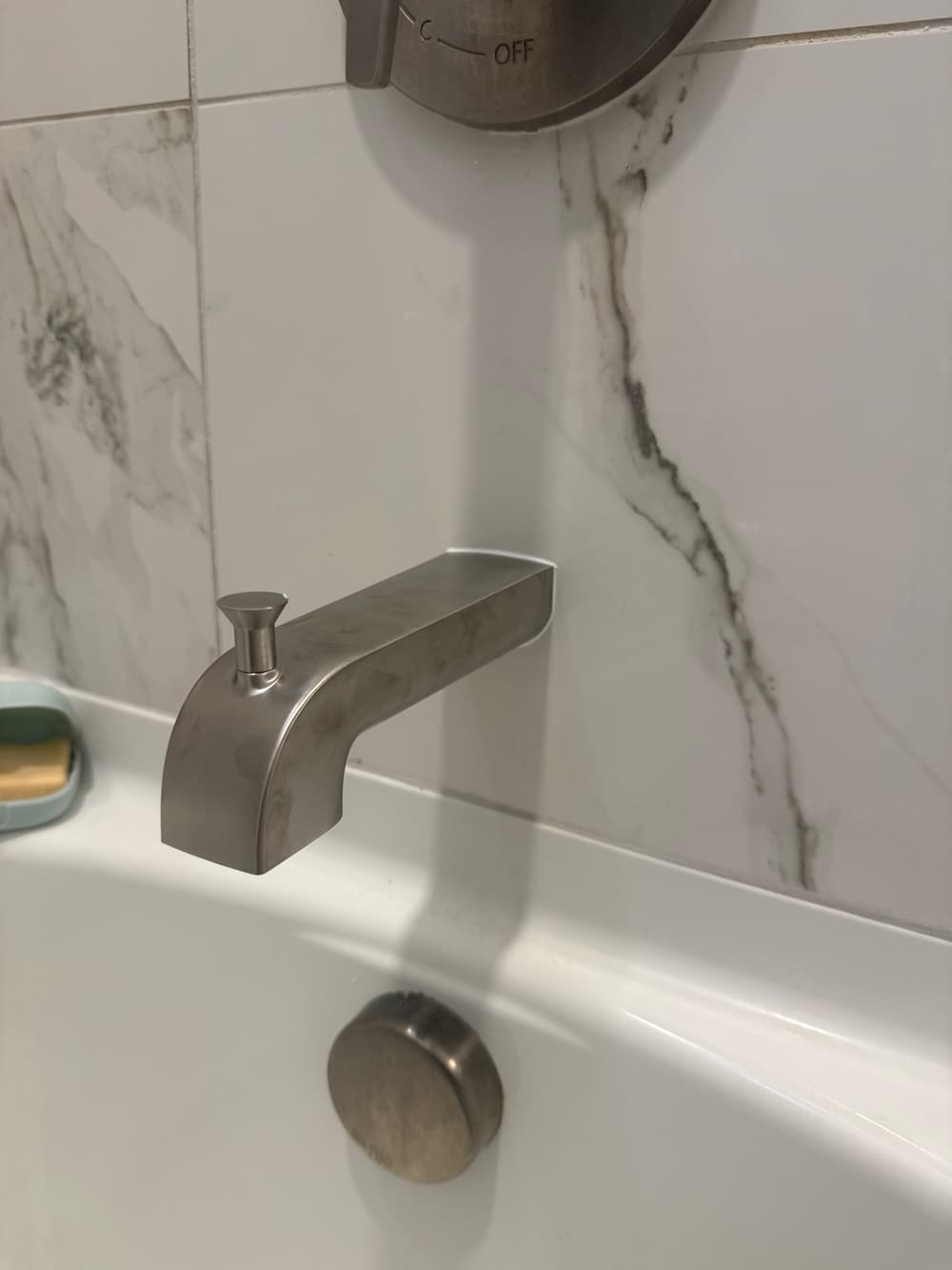 Modern bathtub faucet with sleek design against marble wall background.