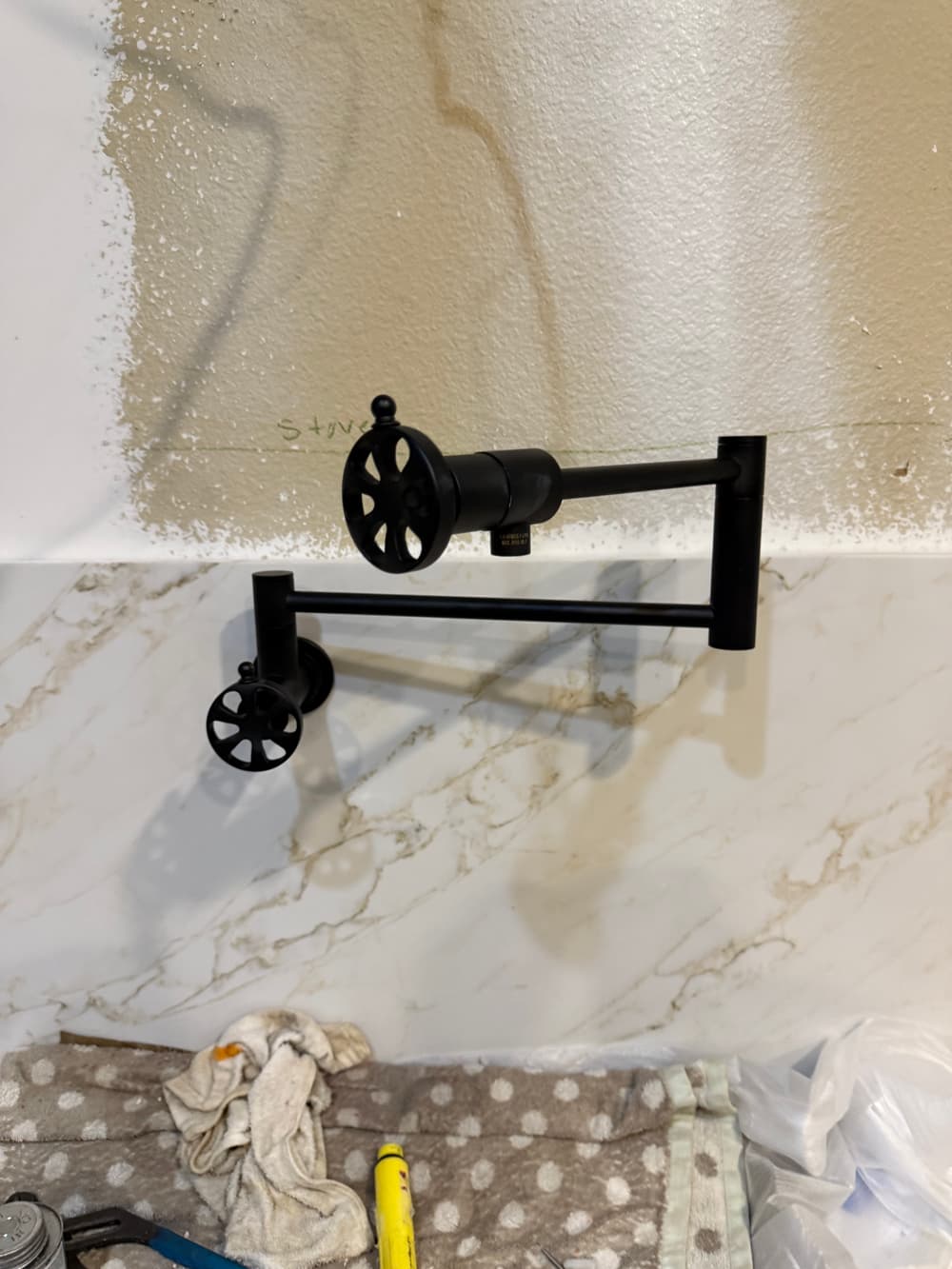 Black industrial wall-mounted faucet with adjustable spouts, installed on a marble backsplash.
