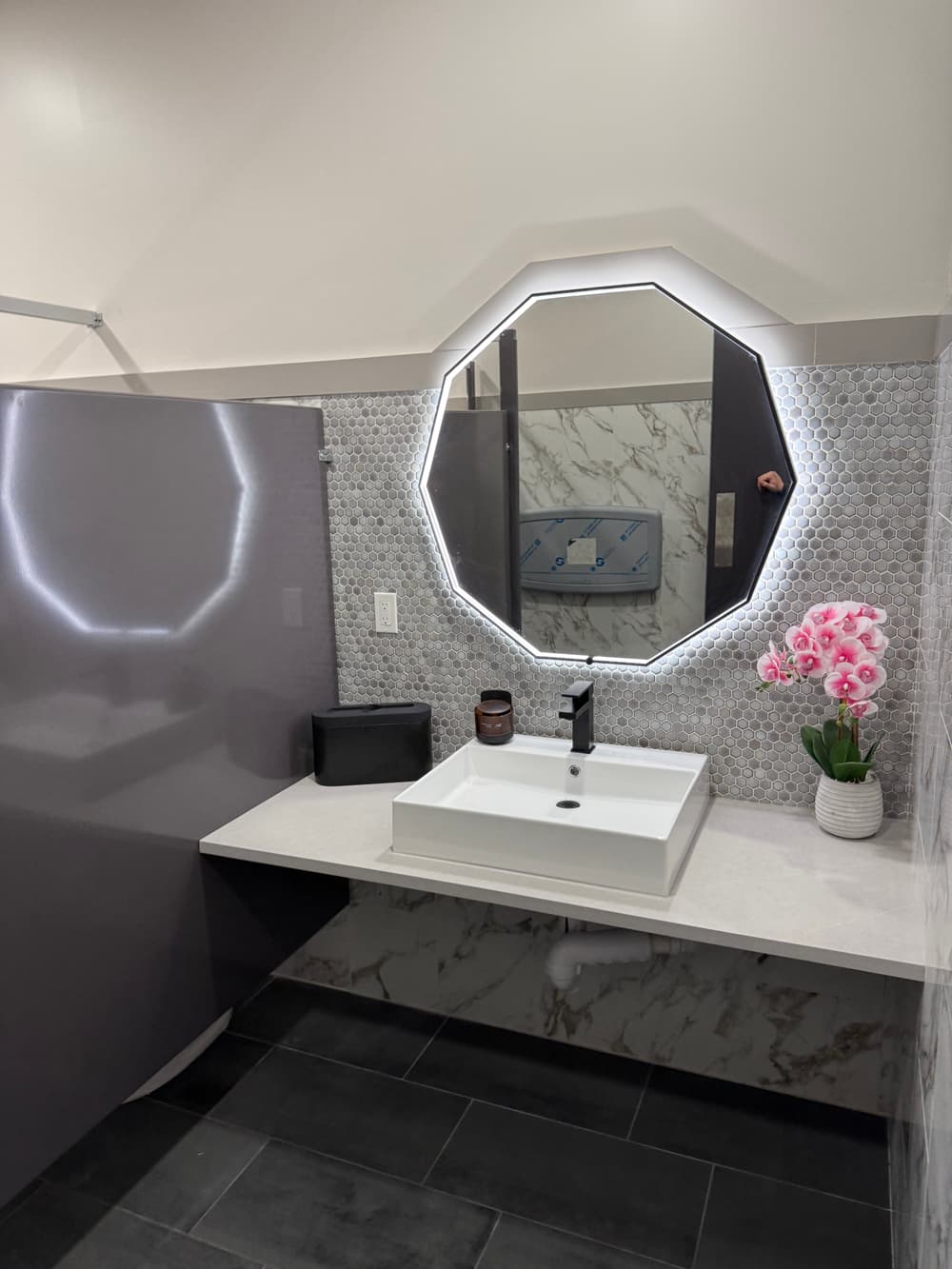 Modern bathroom with octagonal mirror, stylish sink, and pink flowers in a minimalist design.