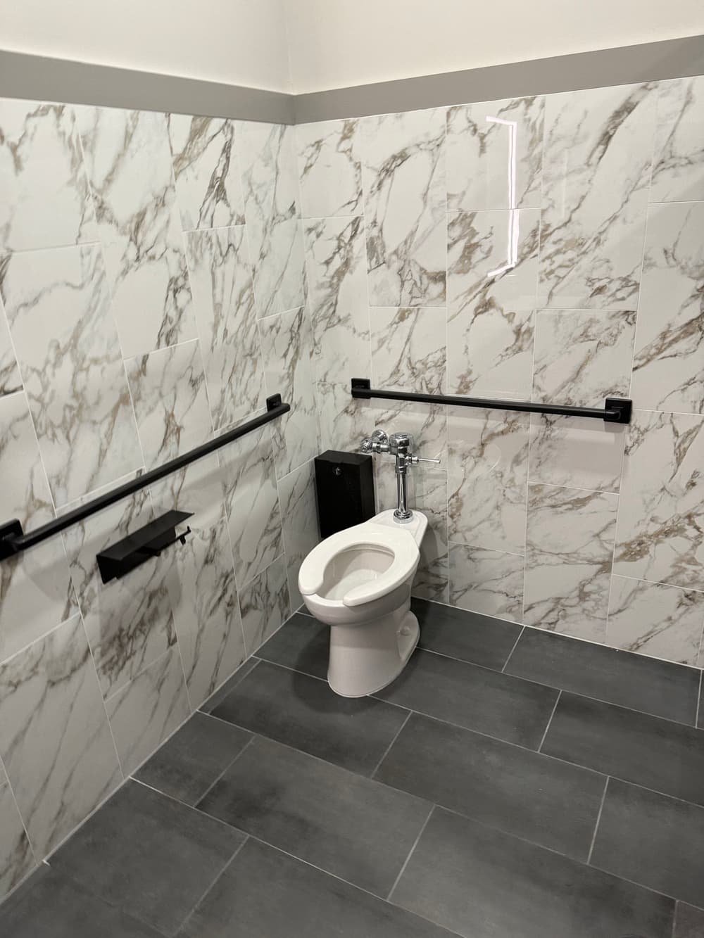 Modern bathroom featuring a white toilet, marble tiles, and accessible grab bars.
